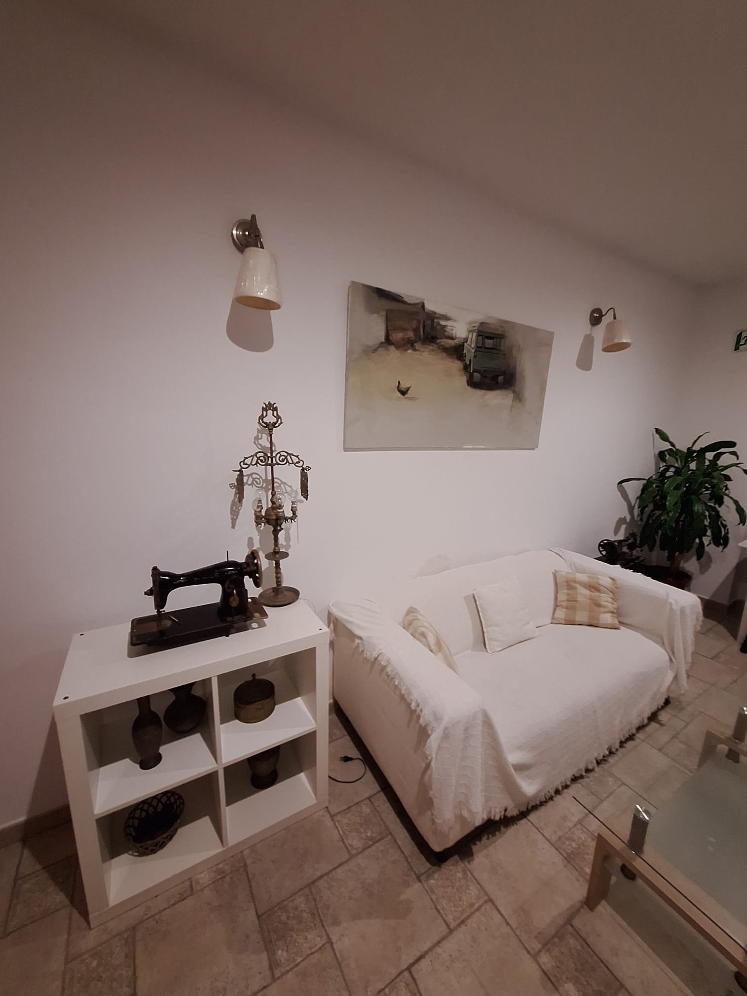 Rincón del salón en Hostal Fenix con sofá, lámparas de pared y una máquina de coser antigua como decoración.