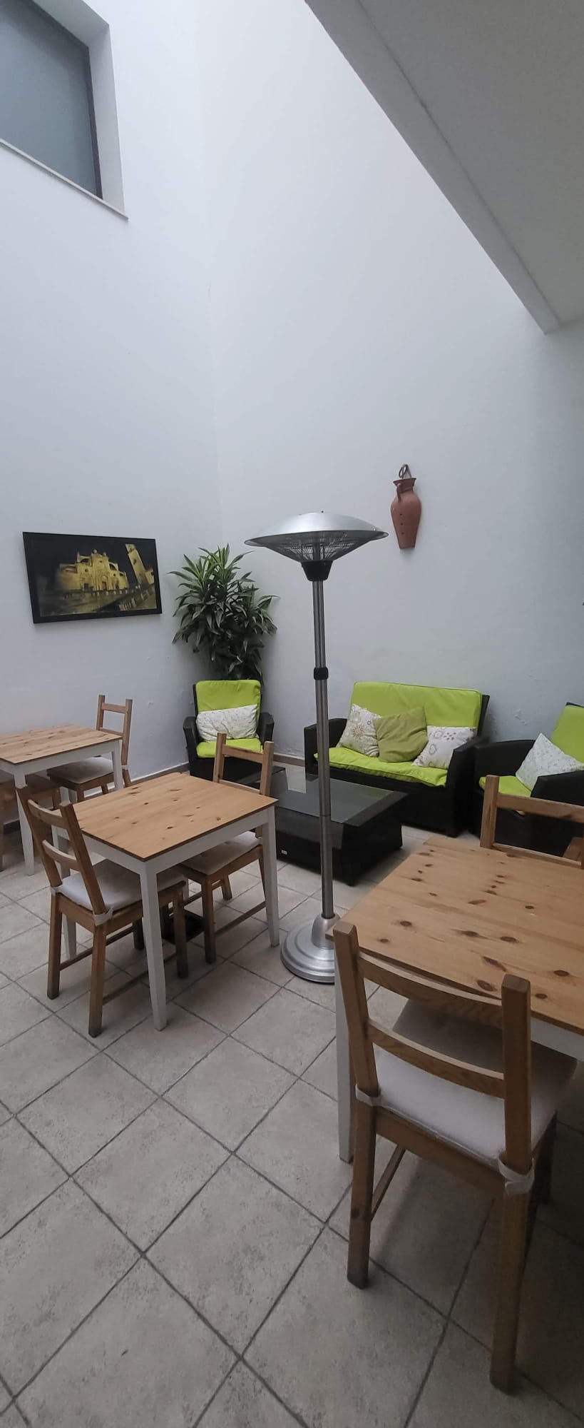 Espacio común en Hostal Fenix con sofás, mesas de madera y decoración en tonos verdes.